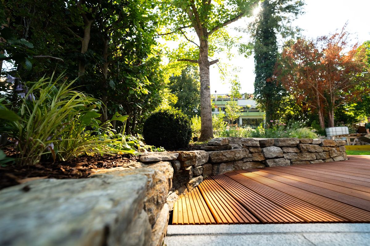 Stone retaining wall, mulched planting bed and clean-edged lawn beside a hardwood deck
